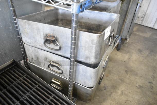 Eight metal pans stacked on a shelf, featuring sturdy handles, used condition, ideal for bulk cooking or catering.