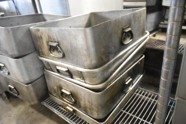 Stack of 8 used metal pans with rectangular shape and sturdy handles, placed on a shelf rack, slight wear visible.