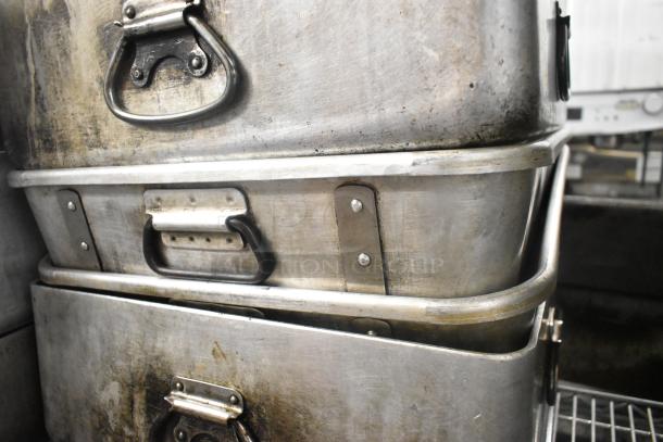 Stacked metal pans with handles, showing wear and patina, indicating heavy-duty use.