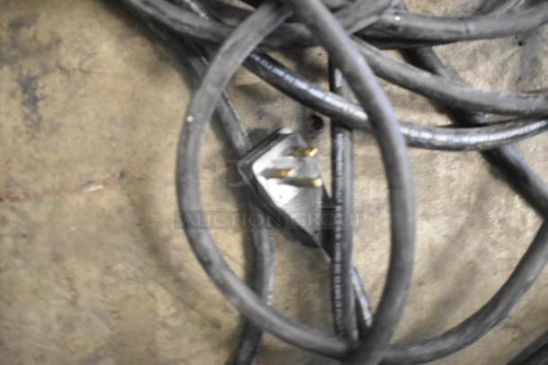 Coiled black power cable on the ground, featuring a metal three-prong plug.