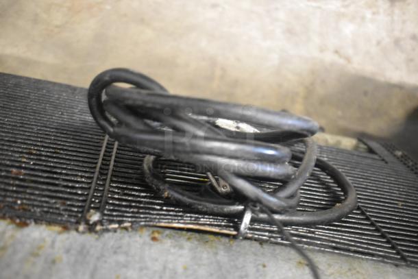 Coiled power cable on the vented top of a 2017 Bison BST-27 stainless steel cooler. Cooler's surface shows wear.