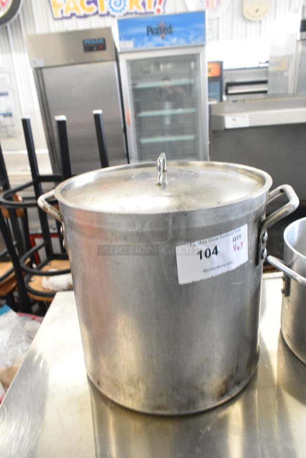 3 metal stock pots with lids, used condition. Auction tag indicates lot 104, quantity 3.