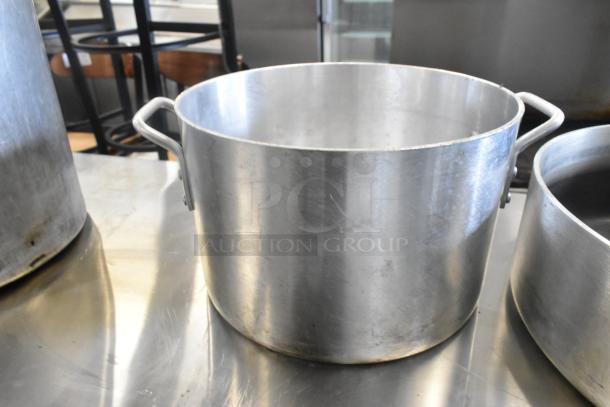 Three metal stock pots with handles, showing signs of use. Ideal for bulk cooking. No visible labels.