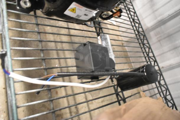 Brand new Cubigel NUT90LR Compressor, 115-127V, with visible scratch and dent. Tags showing voltage and phase details.