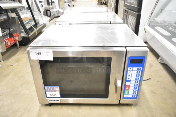 Brand new 2025 Solwave SWA21T stainless steel microwave, medium-duty with push button controls, 208/240V, 1 phase. Scratch and dent condition. USA flag sticker and auction label visible.