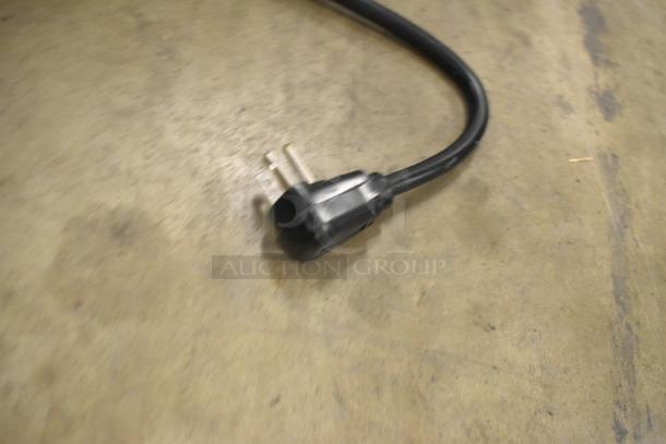 Close-up of a black power plug on a concrete floor, part of the Solwave SWA21T commercial microwave.