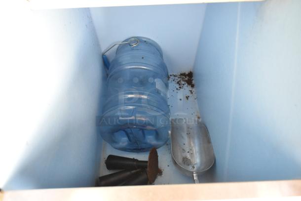 A blue water jug and a metal scoop inside a commercial ice bin with scattered debris.