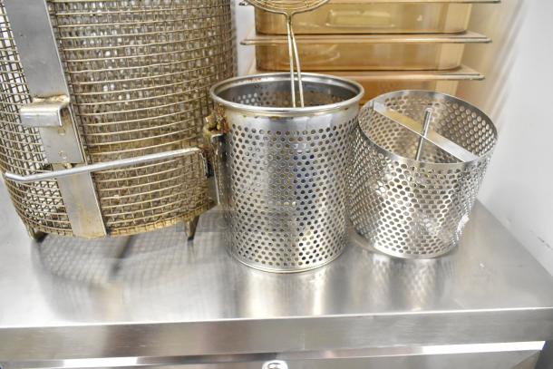Assorted metal fry baskets and poly bins in used condition on a stainless steel surface. 23 items in total.
