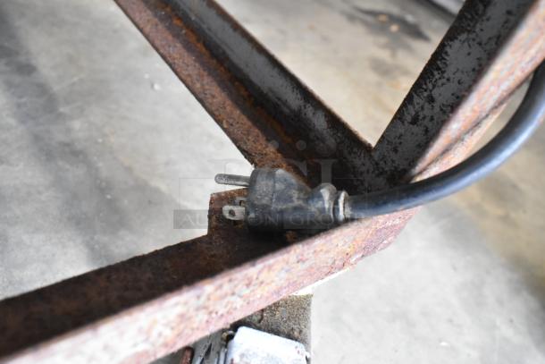 Close-up of a power cord connected to the rusted base of a stainless steel commercial rolled ice cream station on casters. 115 volts, 1 phase.