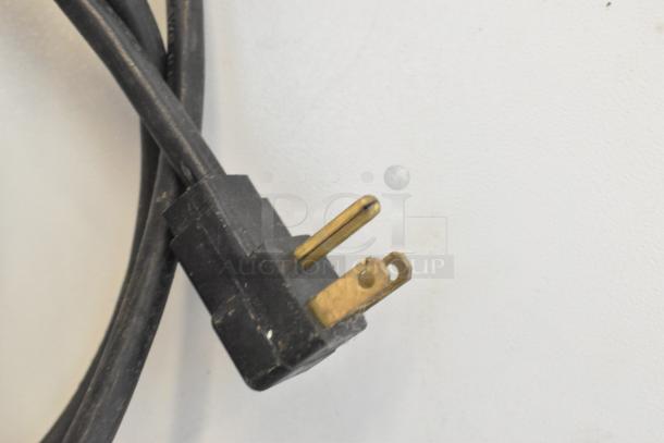 Close-up of the plug of a GEM CTR Metal Mini Cooler Merchandiser, showing its black cable and brass prongs, for 115 volts, 1 phase.