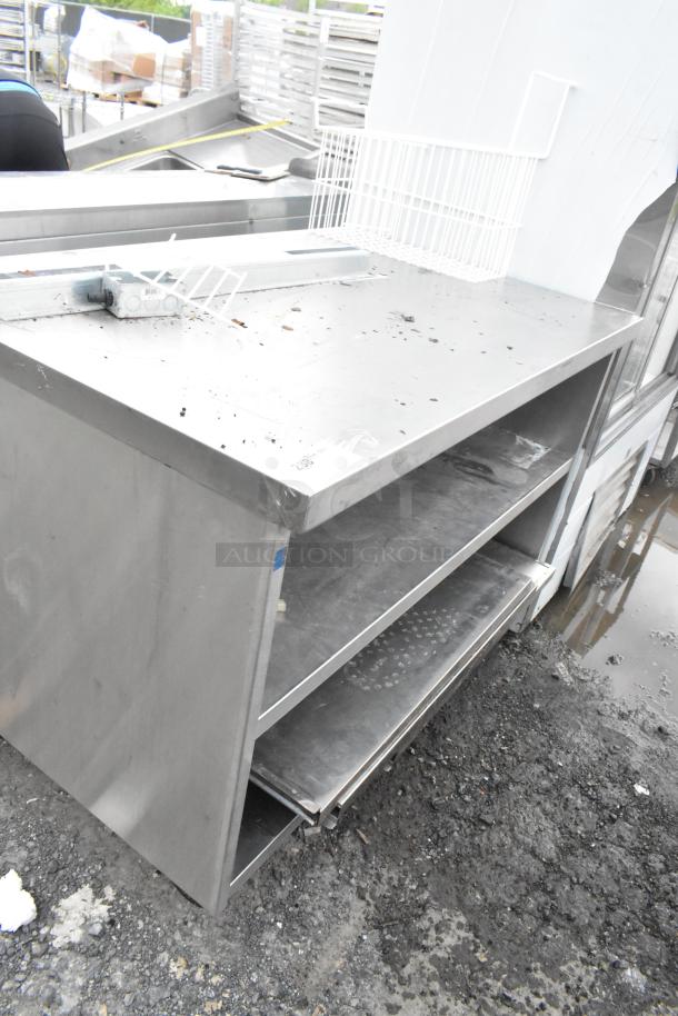 Stainless steel commercial table with two under shelves, on commercial casters. Shows signs of wear, ideal for kitchen use.