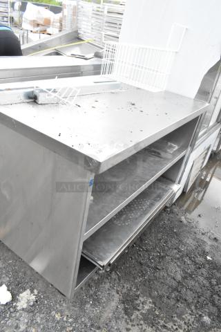 Stainless steel commercial table with two under shelves, on commercial casters. Shows signs of wear, ideal for kitchen use.