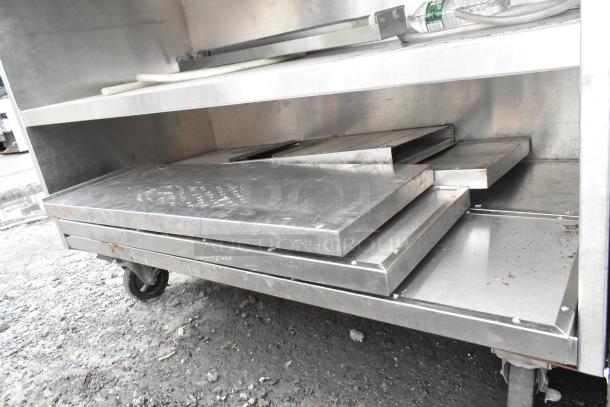 Stainless steel commercial table with two under shelves, mounted on commercial casters. Visible wear, suitable for industrial use.