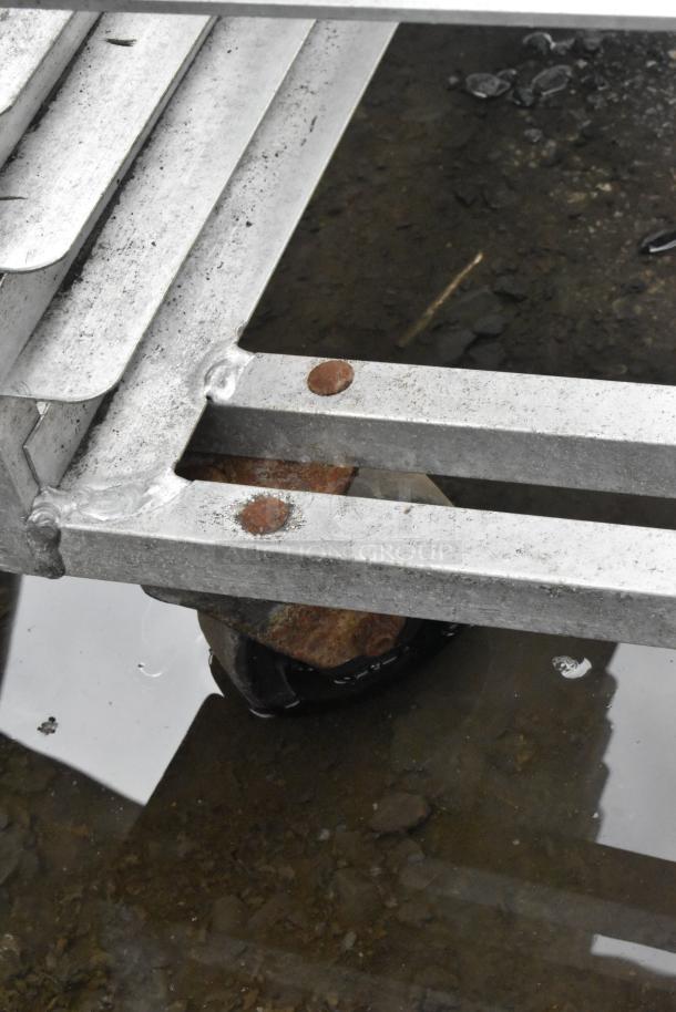 Metal commercial pan transport rack on commercial casters, showing sturdy construction with slight rust on connectors.