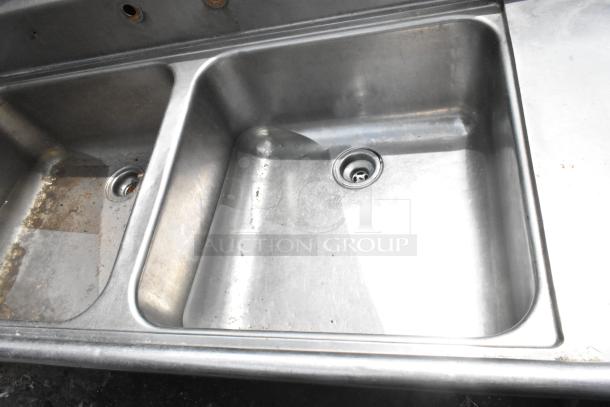 Stainless steel 2 bay sink with dual drain boards, no legs, some wear visible, ideal for commercial use.
