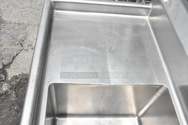 Stainless steel 3 bay sink with dual drain boards. Visible scratches, good condition for commercial use.