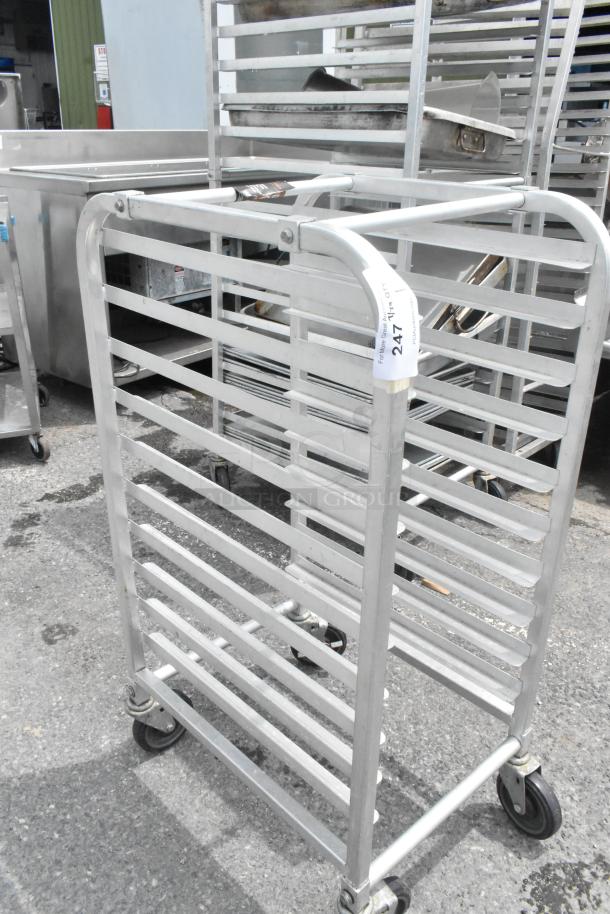 Metal pan transport rack with commercial casters, stainless steel, shows light wear. Marked with "247," ideal for kitchens.