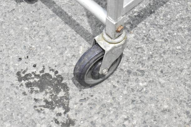 Metal pan transport rack caster, showing robust commercial wheel design on textured concrete.