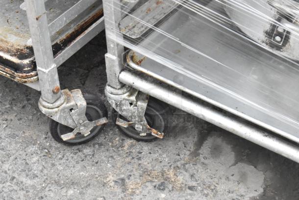 Metal pan transport rack with commercial casters, loaded with 46 full-size baking pans, showing wear on casters.