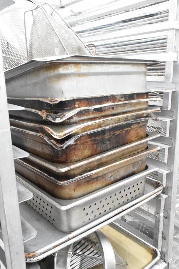 Metal pan transport rack with commercial casters, holding 7 full-size baking pans and 8 drop-in bins, some showing wear.