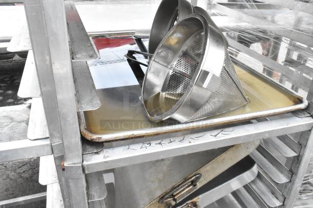 Metal pan transport rack on casters with 7 full-size baking pans and 8 drop-in bins. Visible labels with markings.
