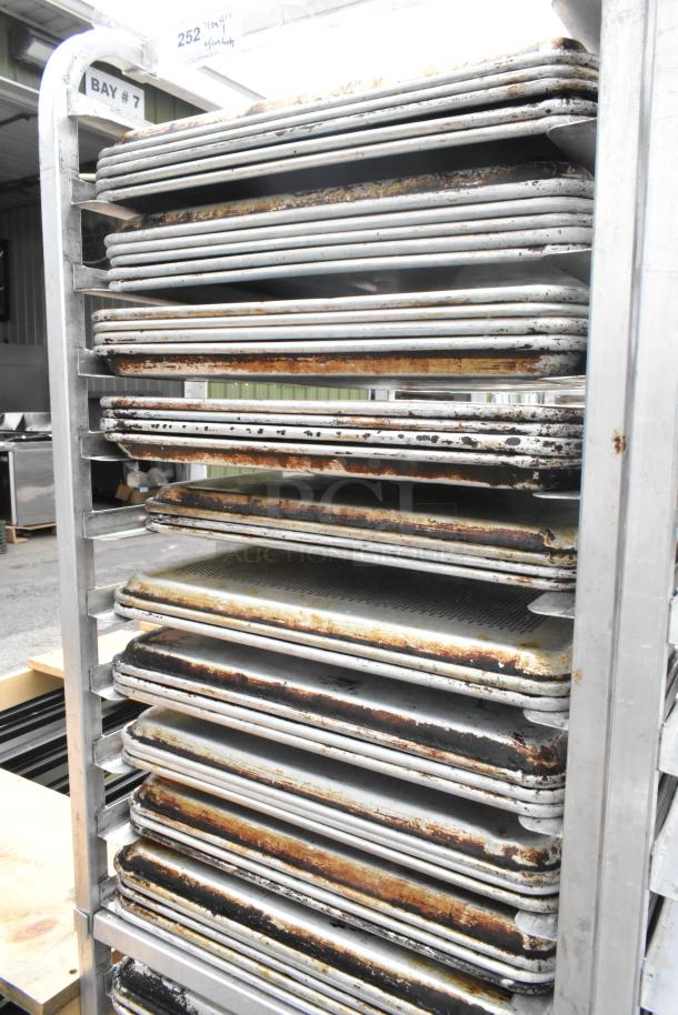 Metal pan transport rack on commercial casters with 40 full-size and muffin baking pans. Used condition, visible wear.