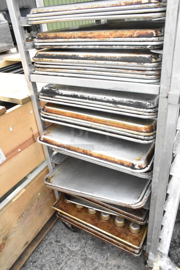 Metal pan transport rack with commercial casters, containing 40 full-size metal baking pans and muffin pans. Some wear visible.