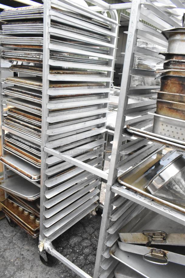 Metal pan transport rack with multiple shelves on commercial casters, holding various baking sheets and pans, in used condition.