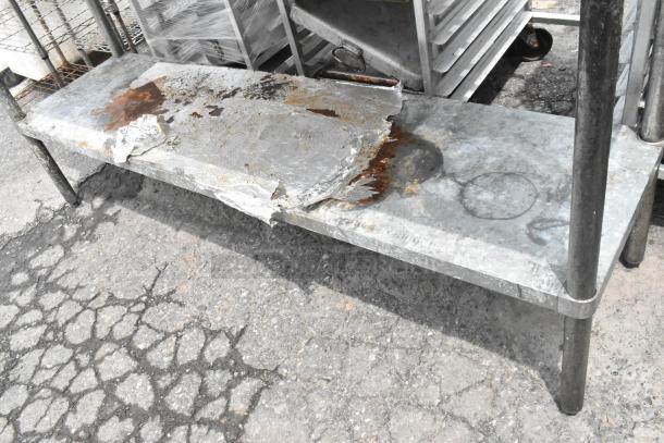 Stainless steel table with metal under shelf, showing wear and rust, placed outdoors.