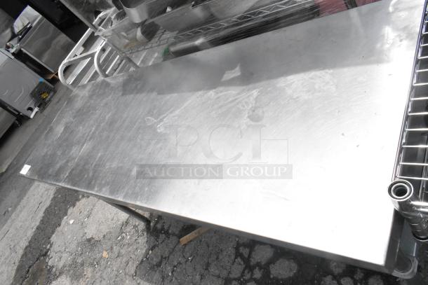 Stainless steel table with metal under shelf, showing light surface wear. Ideal for commercial kitchens or workshops.