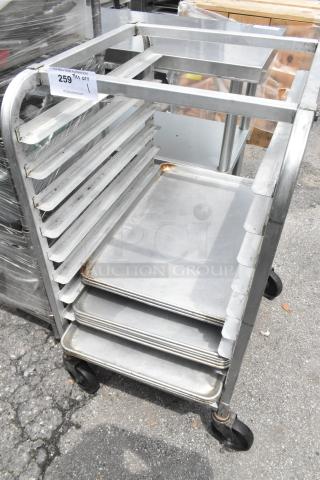 Metal pan transport rack on commercial casters with 11 metal baking pans. Some rust present. Auction tag visible.