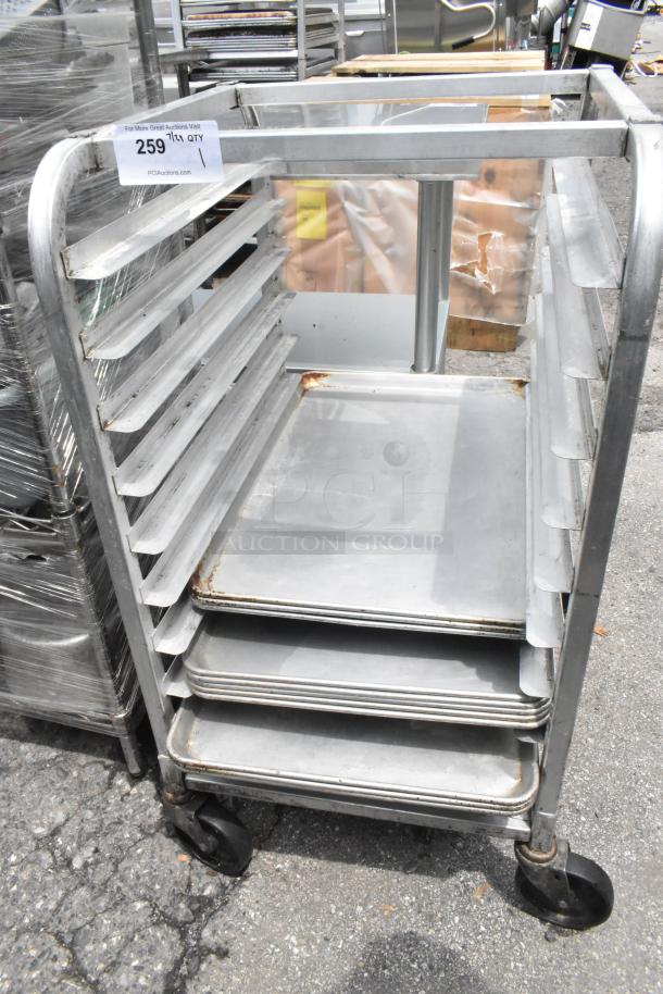 Metal pan transport rack on commercial casters with 11 metal baking pans. Some wear and rust visible. Lot number 259.