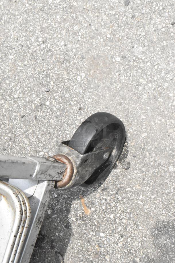 Metal pan transport rack with commercial casters, holding 11 metal baking pans. Slight wear visible on caster.