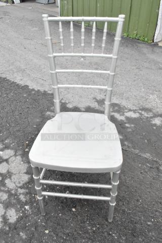 Silver Chiavari stackable banquet chair, showing slight wear, outdoor setting. Ideal for events; 76 chairs available at auction.