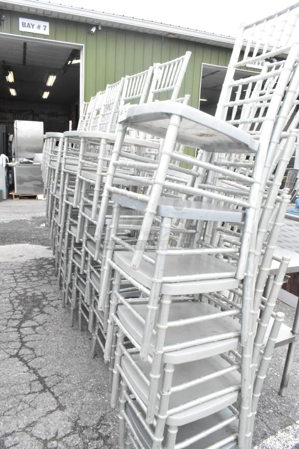 Stack of 76 silver Chiavari stackable banquet chairs, used condition, suitable for events, visible in outdoor setting.