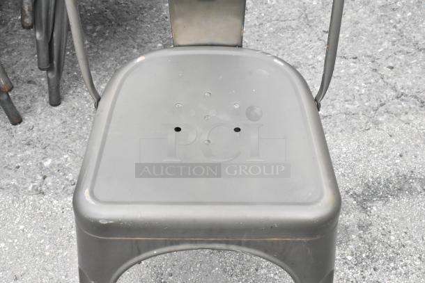 Metal Tolix-style dining chair, gray finish with ventilation holes, some rust marks visible, stackable design, durable use.