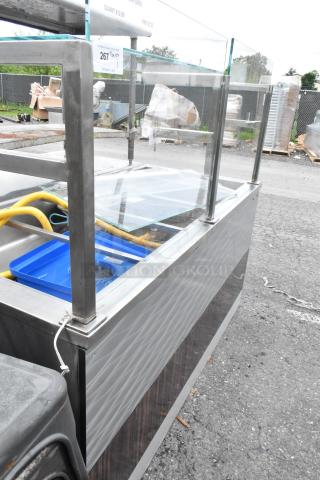 Metal commercial buffet station with sneeze guard, stainless steel frame, glass panels, visible hoses, used condition.