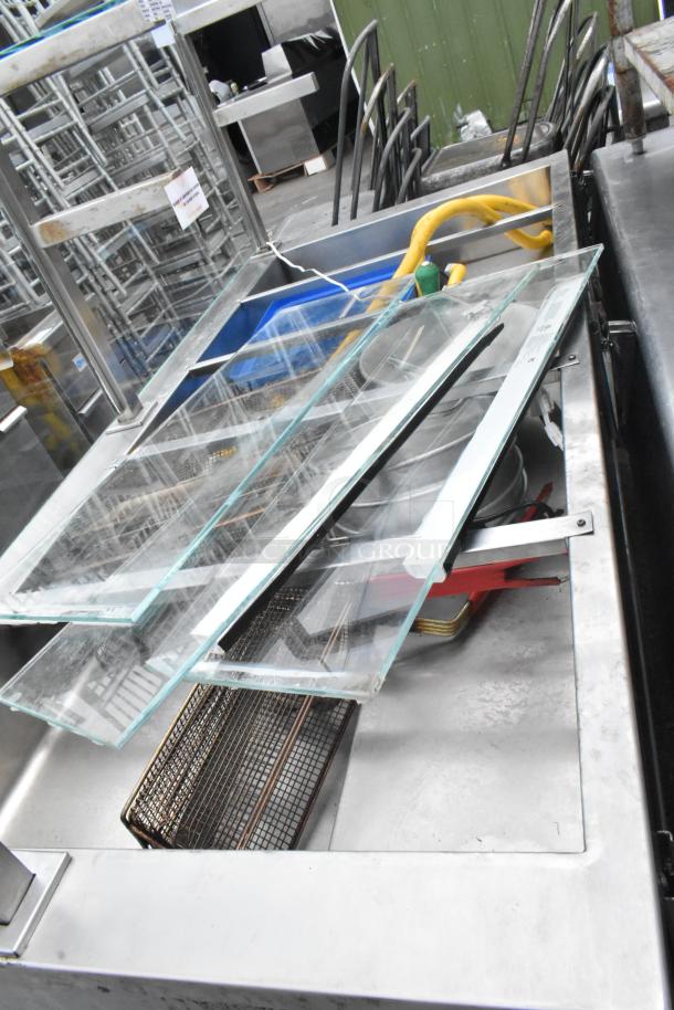 Metal commercial buffet station with sneeze guard, featuring durable glass panels and storage shelves, showing some wear.
