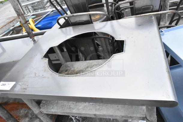 Stainless steel sauce table with central cut-out and two metal under shelves, showing moderate wear and markings.
