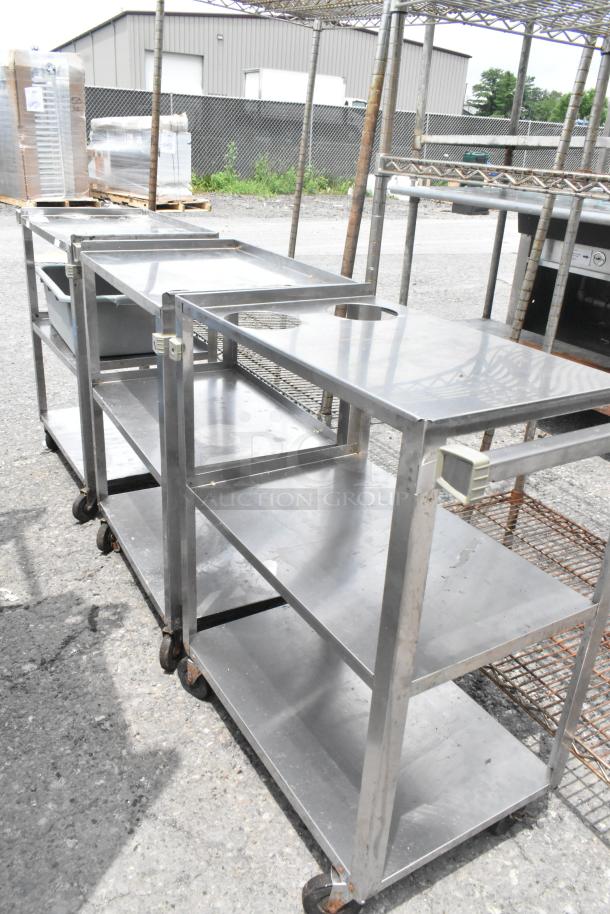 Three stainless steel, 3-tier carts on commercial casters, outdoor setting, fair condition.