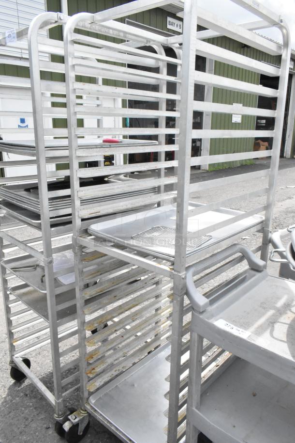 Two metal pan transport racks on commercial casters, used condition, ideal for kitchens, sturdy aluminum frames.