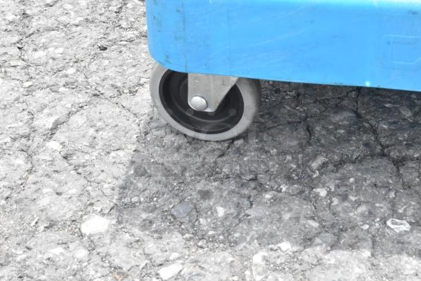Blue poly dolly with commercial caster wheel on rough terrain. Durable plastic material. Excellent condition.