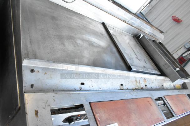 Stainless steel commercial countertop flat top griddle, showing signs of wear, with control knobs and labels visible.