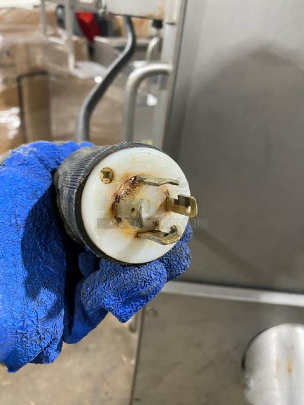 Biro electric meat mixer/grinder power plug, shown with blue glove holding it. Plug shows slight rust. Model on casters.