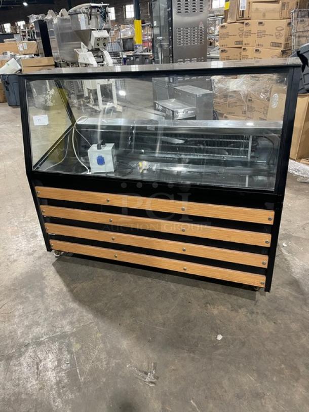 Commercial black slanted glass refrigerated bakery display case with rear prep area, lower storage, and double sliding doors.