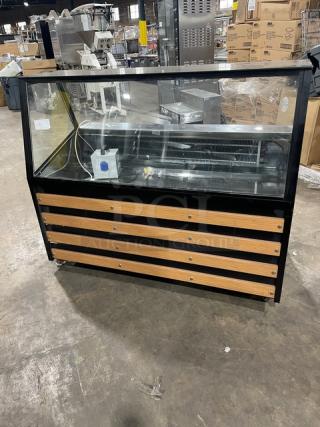 Commercial black slanted glass refrigerated bakery display case with rear prep area, lower storage, and double sliding doors.