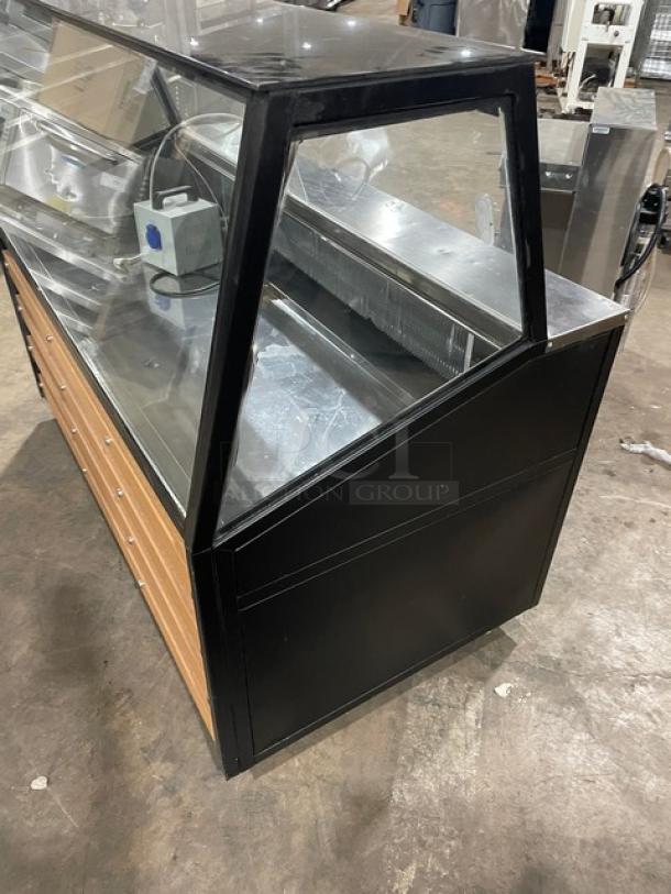 Commercial black slanted glass refrigerated display case with rear prep area, lower storage, and double sliding doors on casters.