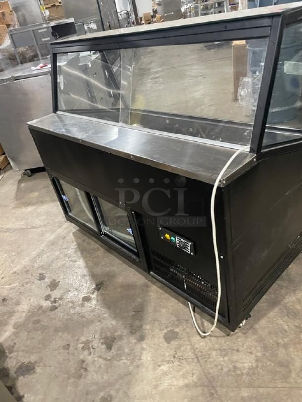Commercial black slanted glass refrigerated display case with rear prep area, lower storage, double sliding doors, on casters.
