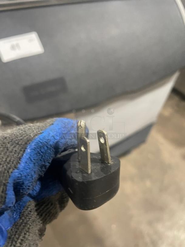 Ice-O-Matic ICEU300FA2 plug close-up, showing a standard 115V connector. Gloved hand holding plug in front of the machine.
