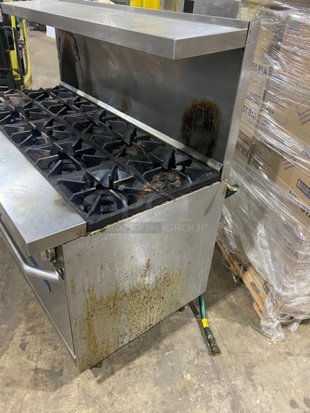 Bakers Pride stainless steel 10 burner range with double oven, model 60BP10BS26N. Features backsplash, overhead salamander shelf, wired oven racks, and gas connection hose. Standing on legs. Used condition.